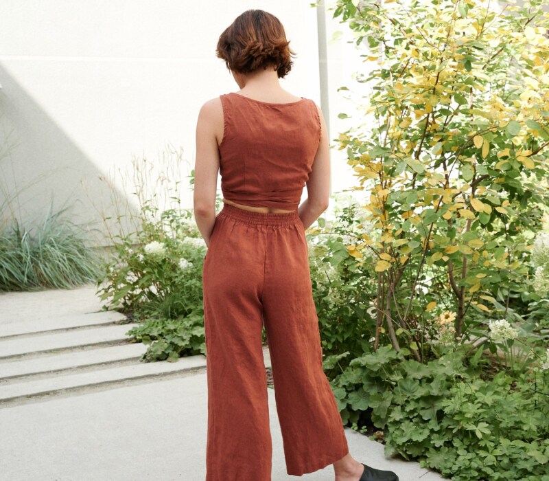 Model is wearing wide leg linen trousers in terracotta color