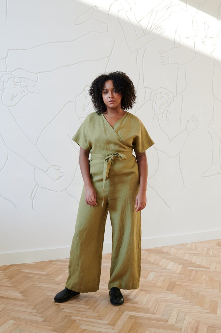 Front of a model wearing an olive linen jumpsuit with dropped shoulders and a plunging V-neck