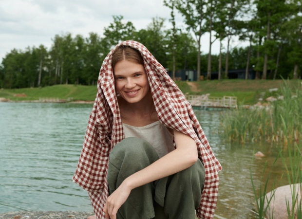A woman squatting in green linen trousers and a terracotta linen shirt over her head and shoulders
