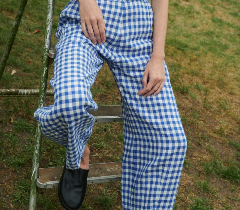 model sitting outside wearing blue gingham linen set of relaxed trousers and V-neck summer wrap top