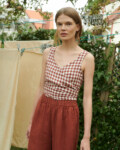 model in a garden wearing gingham linen summer top in V-neck and wide leg linen trousers