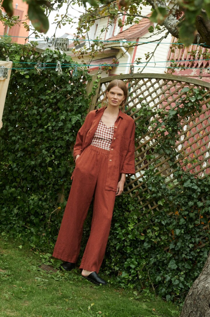 model in a garden wearing a terrracotta gingham linen wrap top and wide leg linen trousers and shirt in terracotta linen