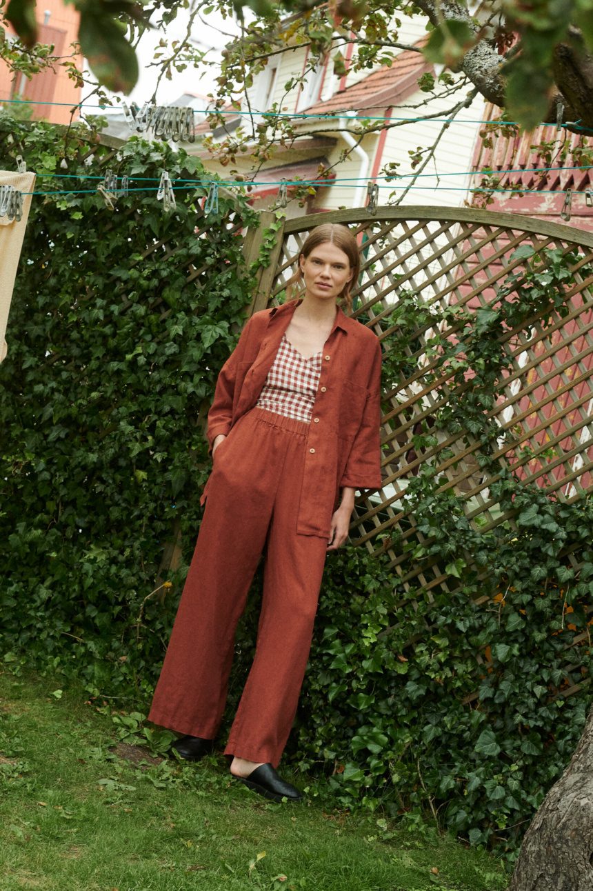 model in a garden wearing a terrracotta gingham linen wrap top and wide leg linen trousers and shirt in terracotta linen