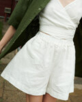 woman wearing natural linen wide summer shorts in milky white and v-neck wrap top along with forest green shirt