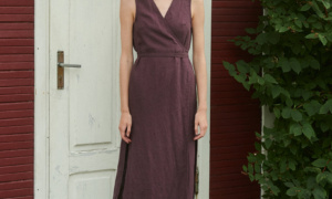 model wearing a V-neck linen wrap dress in eggplant violet with side slits and midi length while standing outside summer house