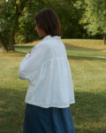 Woman wearing a flowy linen white top with ruffled back detail and a blue linen wool blend skirt