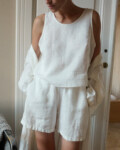 Woman in a relaxed white linen outfit, including a sleeveless top and matching shorts, as well as a lightweight linen robe