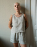 Model wearing a sleeveless top in natural grey linen with a rounded neckline and cropped length, paired with matching shorts, creating a relaxed loungewear look