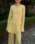 Model wearing a butter-yellow linen three-piece set, including a tailored button-down blouse with a bold oversized collar, an asymmetrical layered skirt panel, and relaxed wide-leg trousers