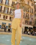 Model in white fitted tank top paired with butter yellow wide leg linen pants featuring a wrap-style front panel with drawstring ties at the waist