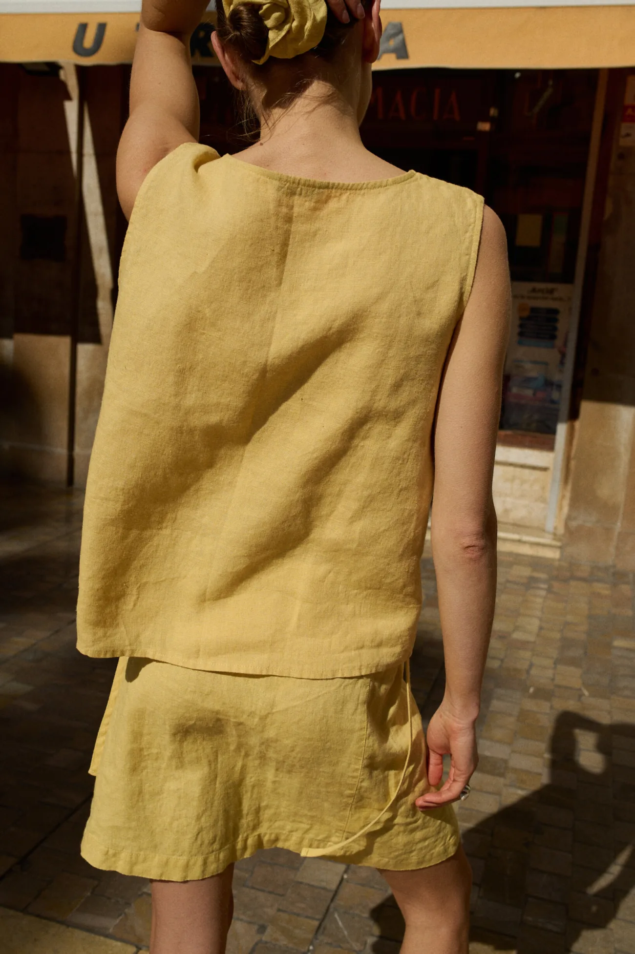 Woman wearing a sleeveless, loose-fitting butter-colored linen top paired with a matching mini skirt