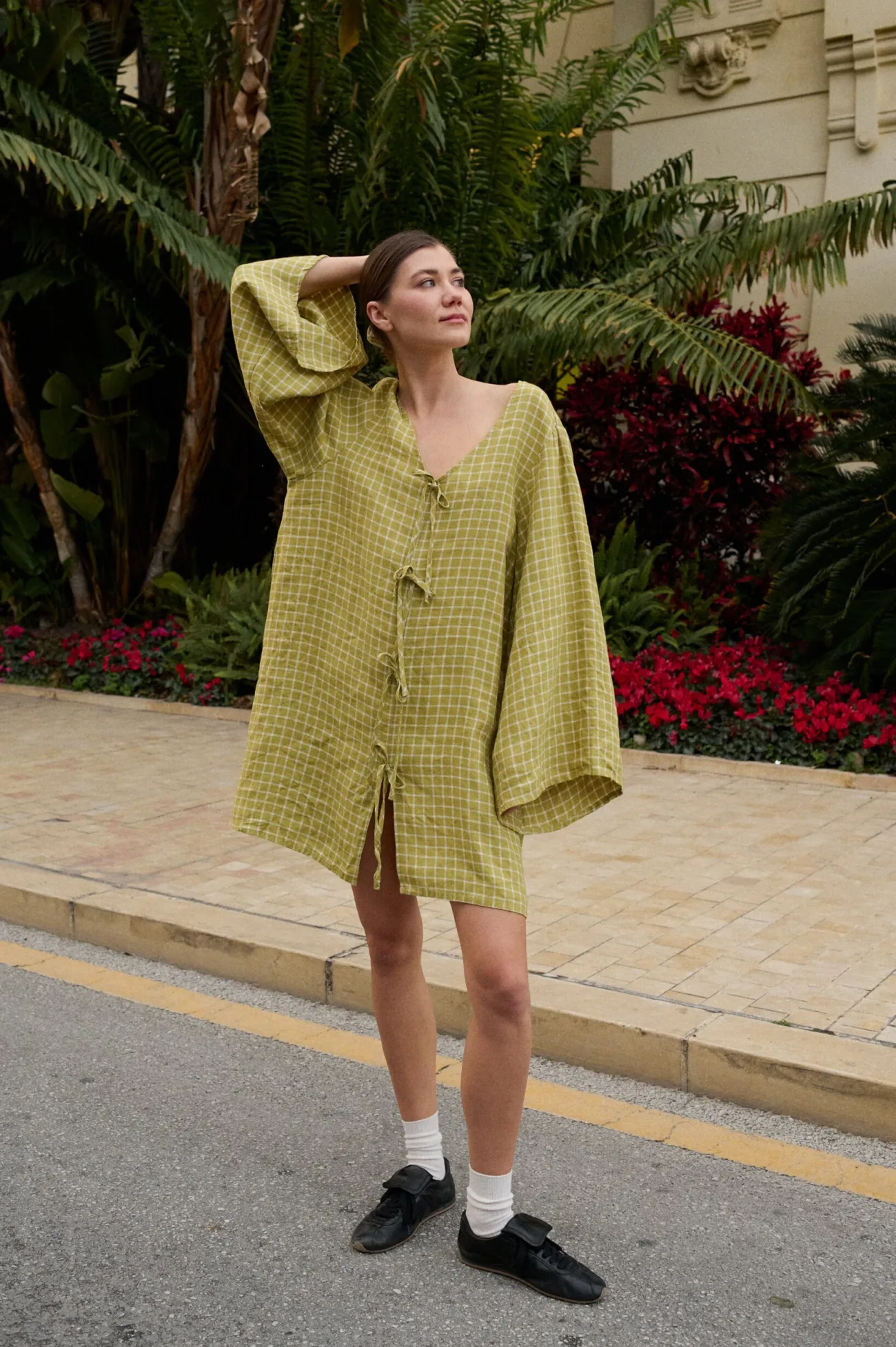 Model wearing a relaxed pickle checks linen dress with a deep V-neckline, decorative tie closures down the front, wide long kimono-style sleeves, and a mid-thigh length