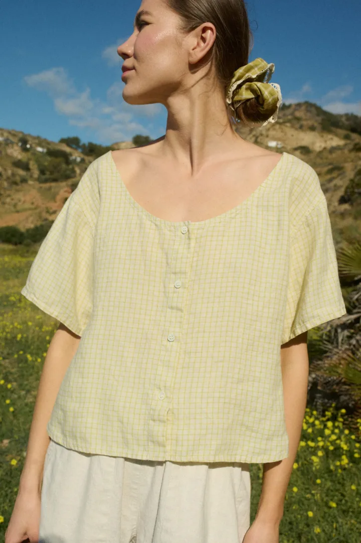 A short-sleeved, button-up top in apple checks linen, featuring a slightly relaxed fit, scoop neckline, and full-length buttons down the center front