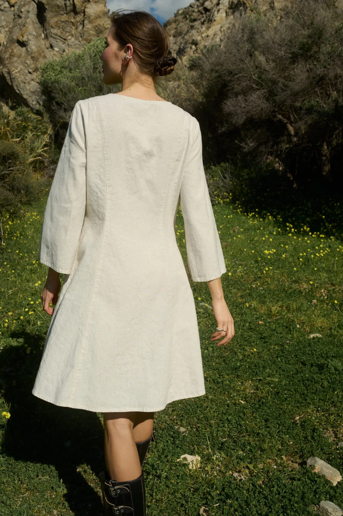 Model seen from the back, wearing a white cotton blend dress with three-quarter length sleeves that flare slightly at the ends and an A-line silhouette that gently flares from the bodice to a knee-length hem