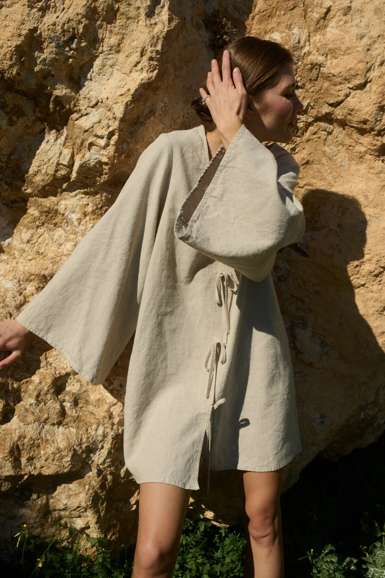 Model showcasing a natural cotton-linen blend mini dress with a deep V-neckline, decorative front tie-bow details, wide shoulders, flowy sleeves, and a relaxed A-line silhouette