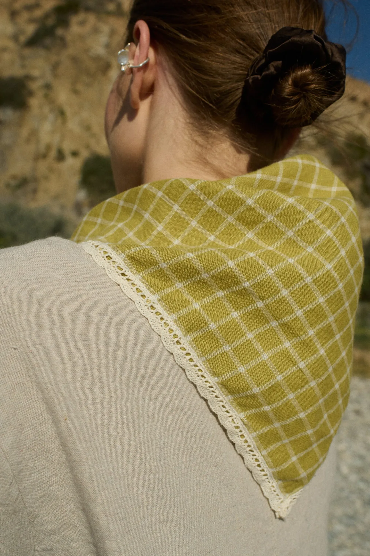 Model wearing a linen bandana in a pickle checks pattern with delicate white lace trim, tied around her neck