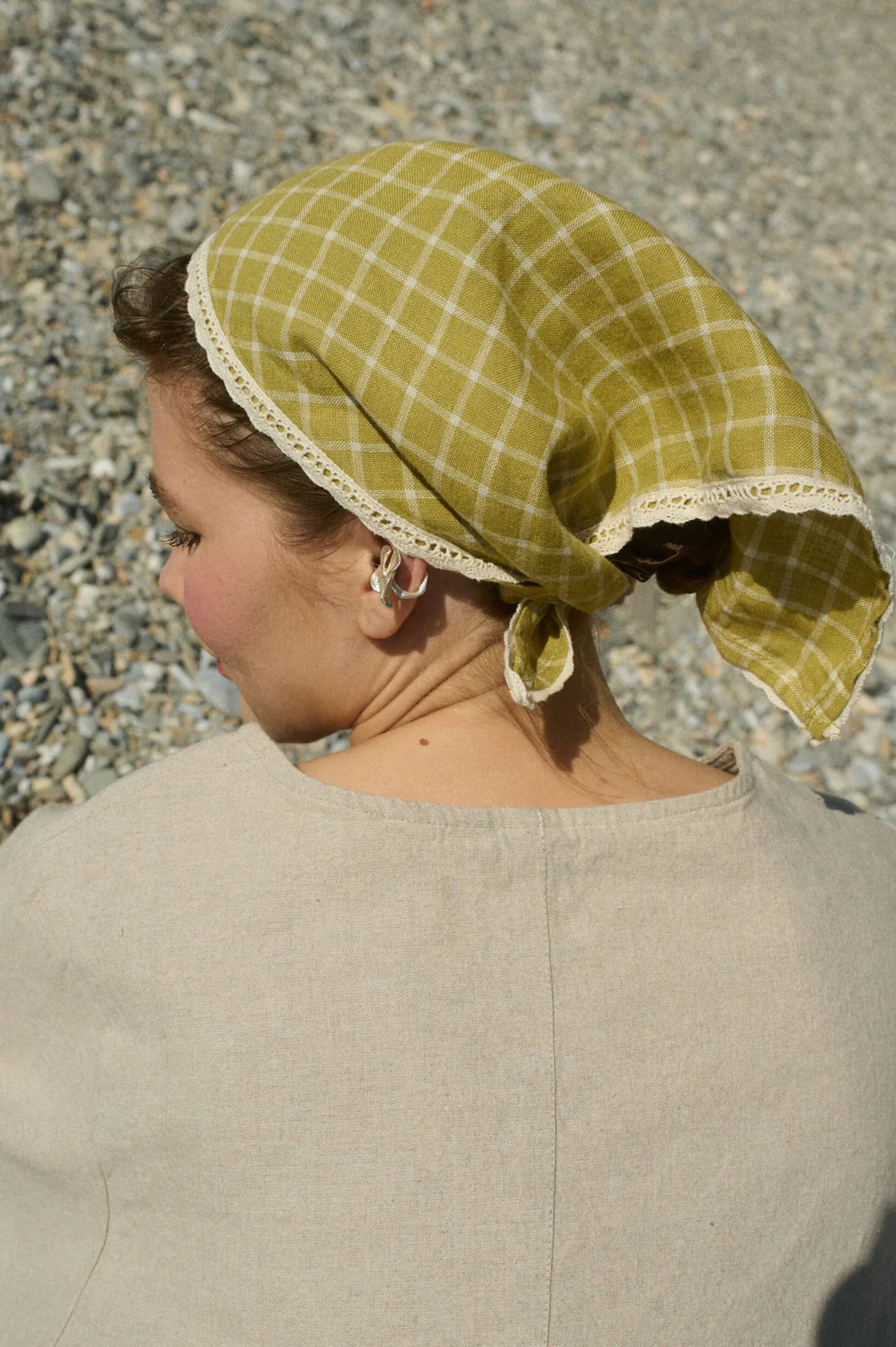 Model wearing a linen bandana in a pickle checks pattern with delicate white lace trim, tied around her head