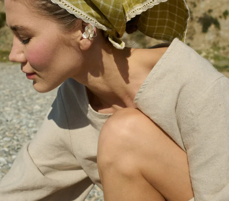 Model wearing a linen bandana in a pickle checks pattern with white lace trim, tied around the head, paired with a natural cotton blend dress