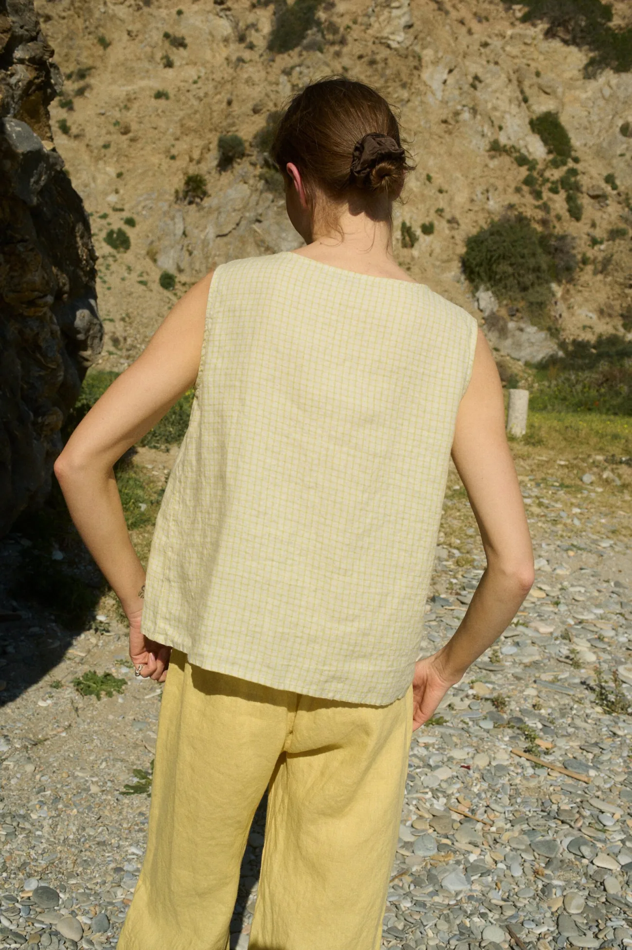 Model seen from the back, wearing a relaxed fit sleeveless top in soft apple checks linen, paired with wide-leg butter-yellow linen pants