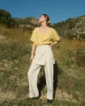 Model in nature wearing a bright yellow linen top and cream linen-cotton blend wide-leg pants with a wrap-around panel detail