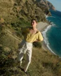 Model wearing a short-sleeved butter-yellow linen button-up top with a wide scoop neckline, tucked into flowing white cotton-blend wide-leg pants with a unique overlapping skirt panel