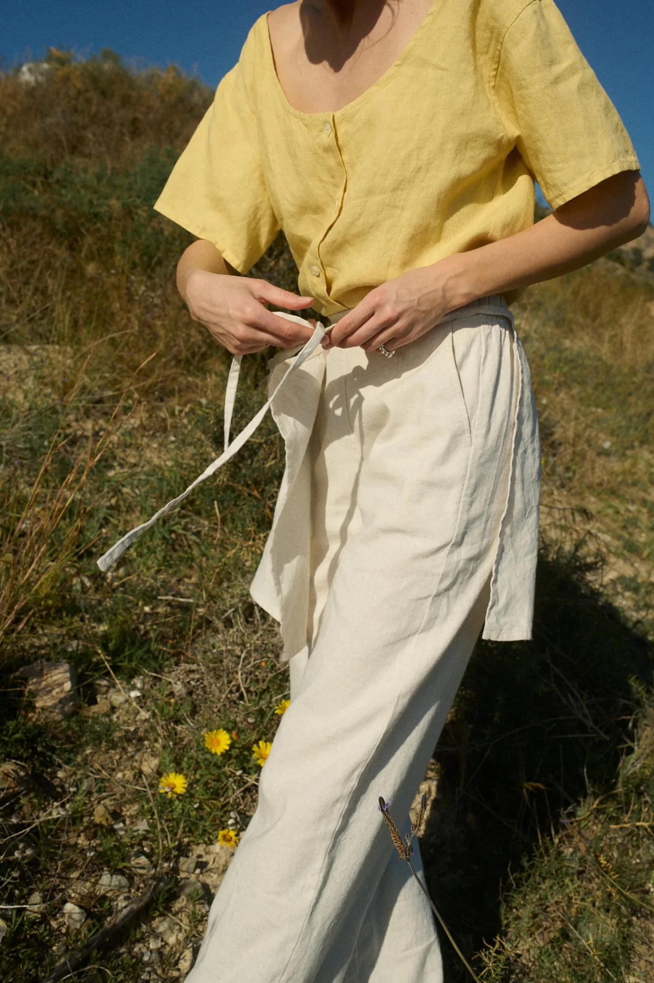 Close-up of the naural grey linen-cotton wrap tie at the waist, highlighting its layered design over wide-leg pants, paired with a structured yellow linen top