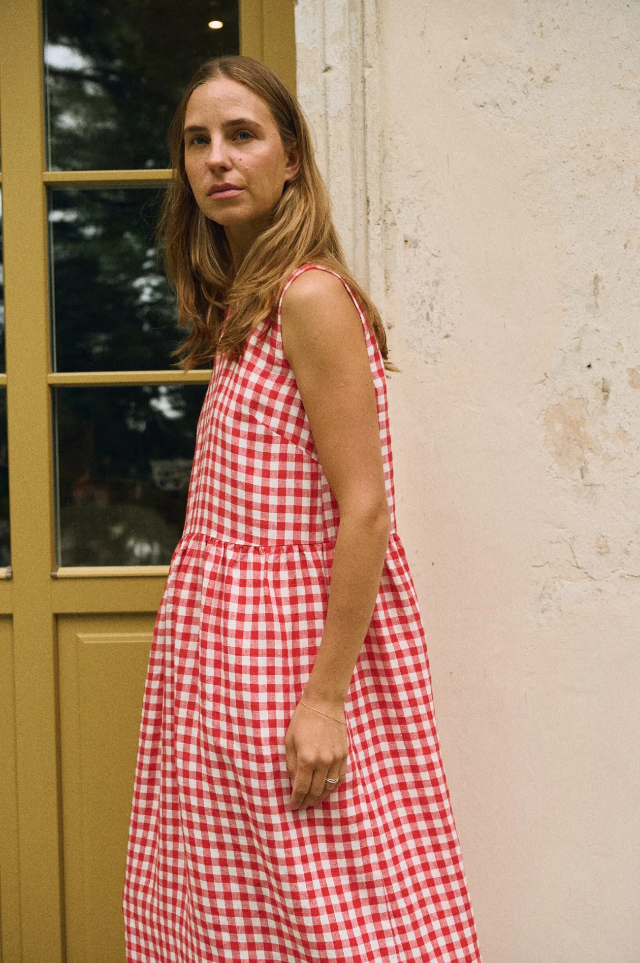 A woman dressed in a sleeveless red and white gingham linen dress featuring a drop waist