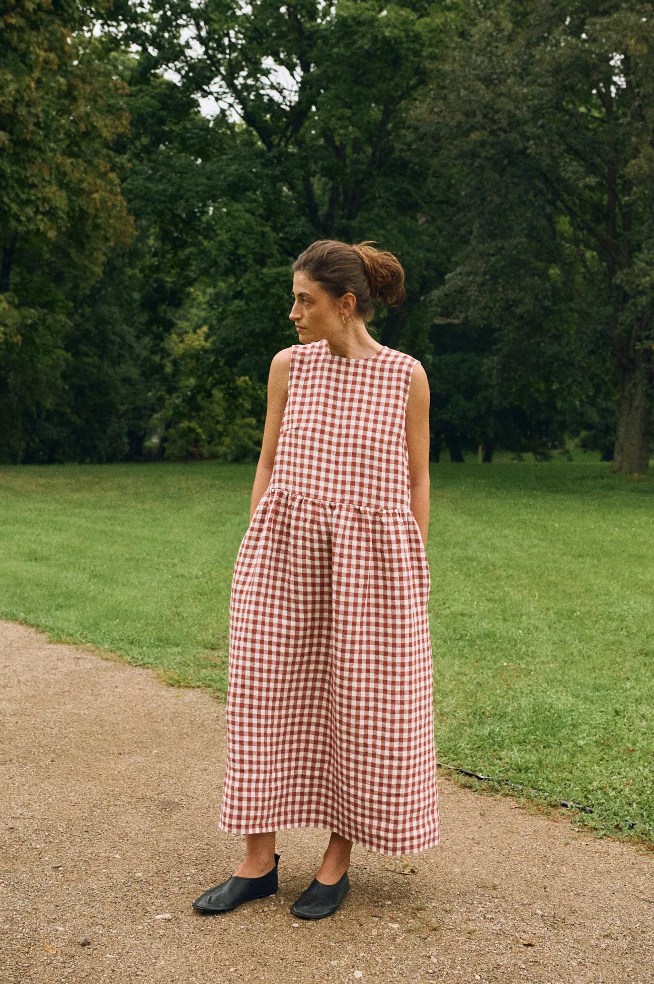 Woman wearing a sleeveless terracotta gingham linen dress with a drop waist, gathered maxi-length skirt and pockets