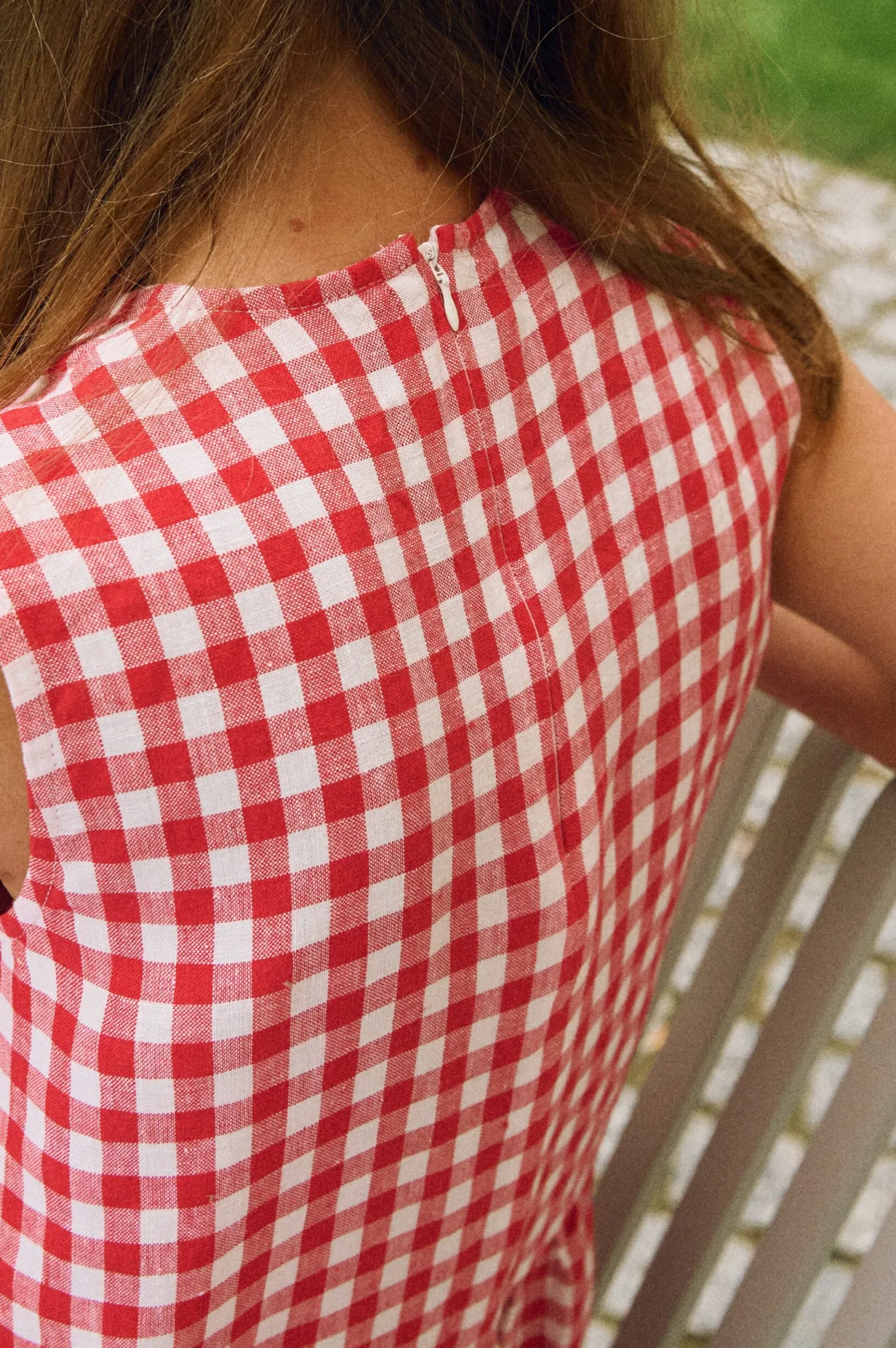 Top portion of a sleeveless red and white gingham linen dress with a back zipper