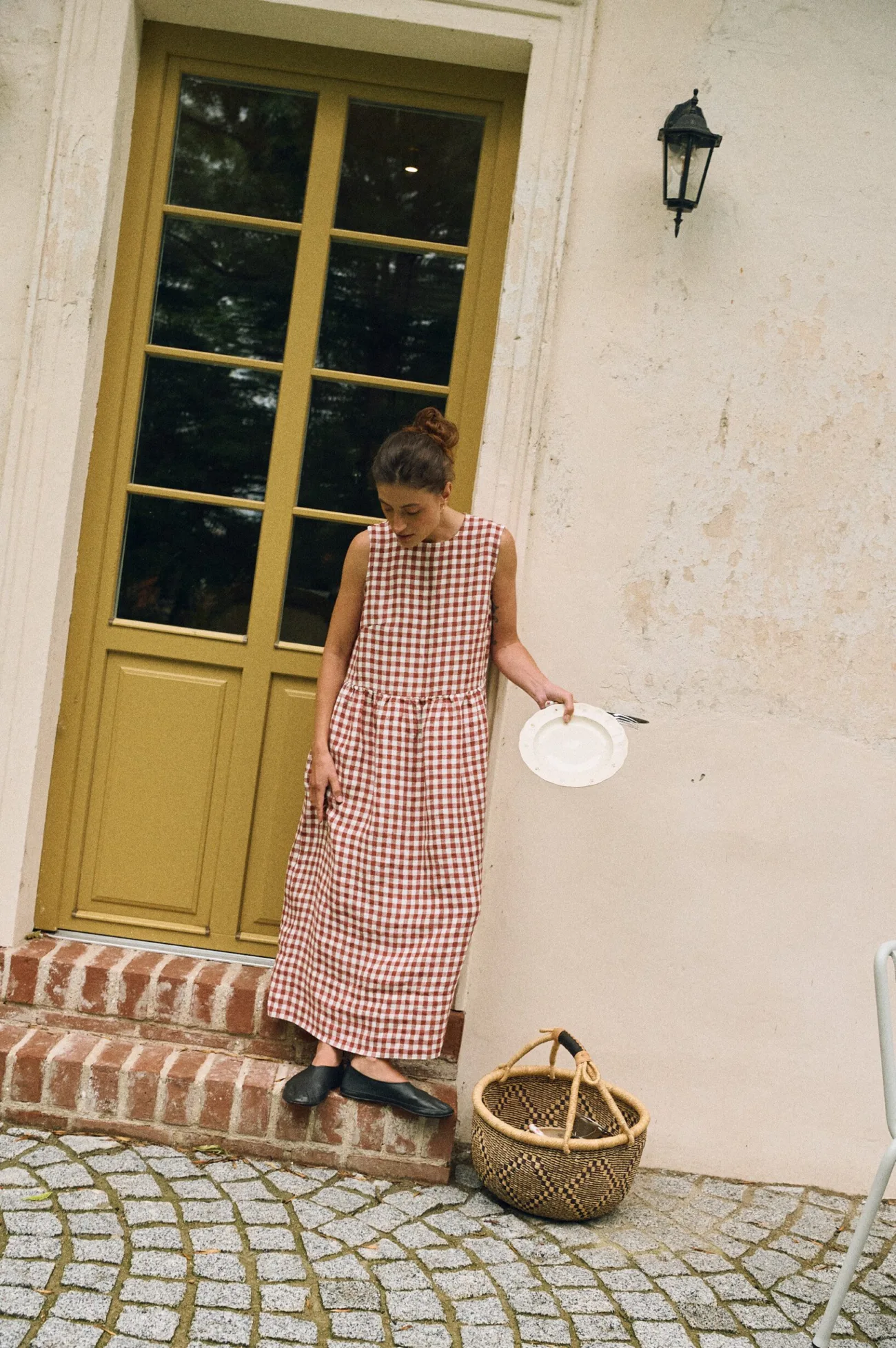 Woman wearing a sleeveless terracotta and white gingham linen maxi dress, with a gathered waist and a flowing long skirt