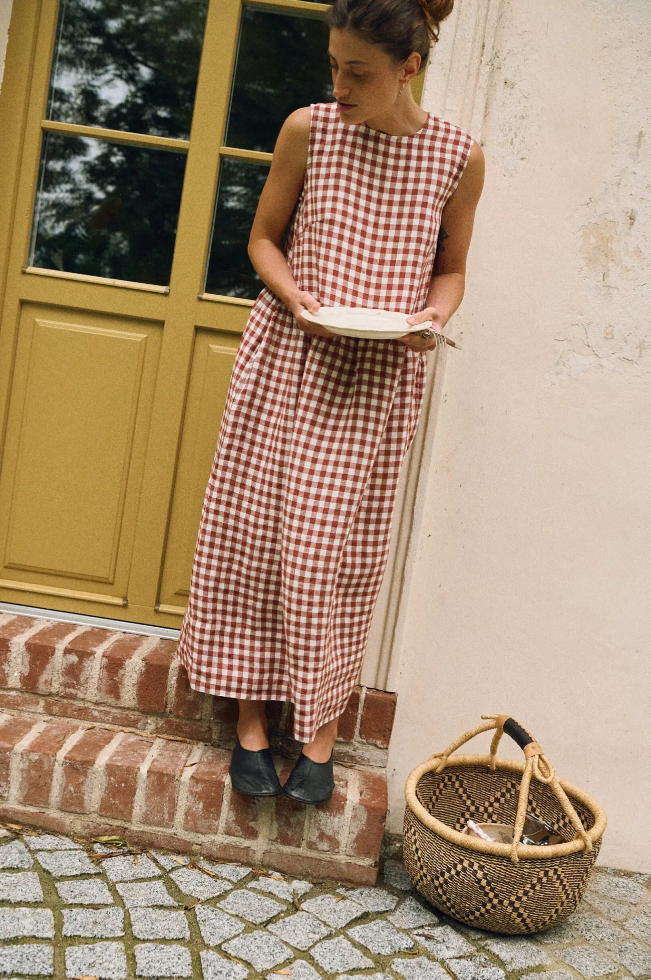 Woman wearing a sleeveless terracotta and white gingham linen maxi dress, featuring a gathered waist and flowing skirt
