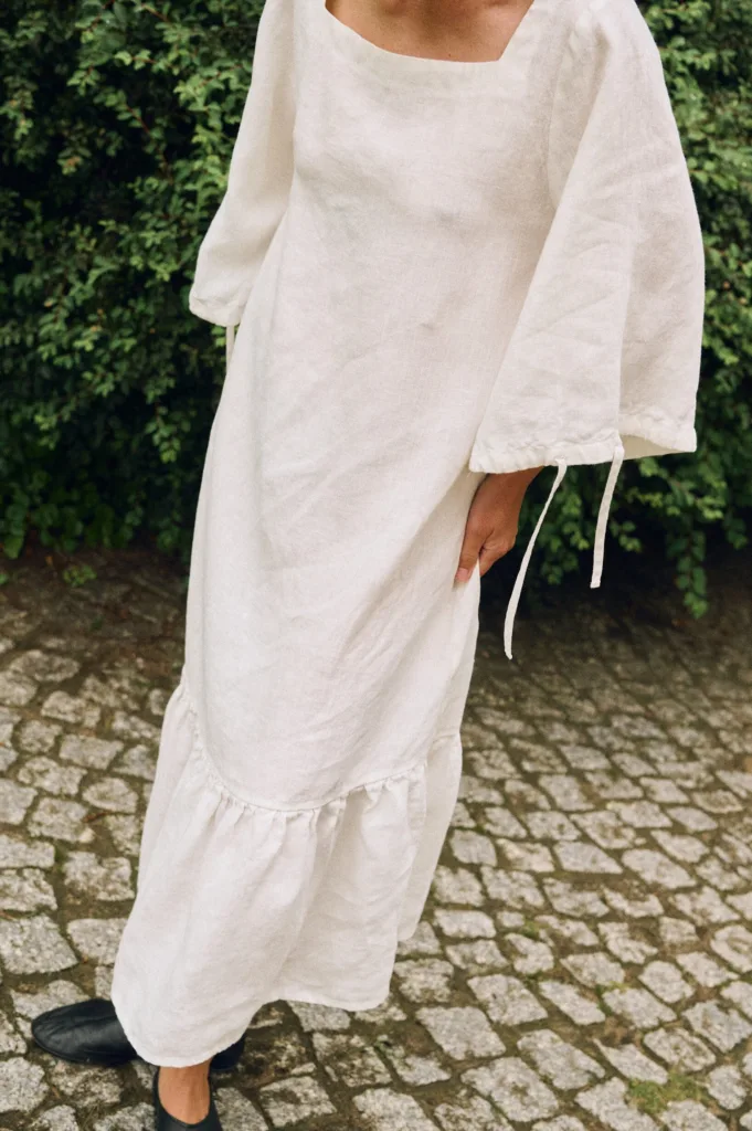 Close-up of an off-white linen dress highlighting the square neckline, wide sleeves with ties, and ruffled hem