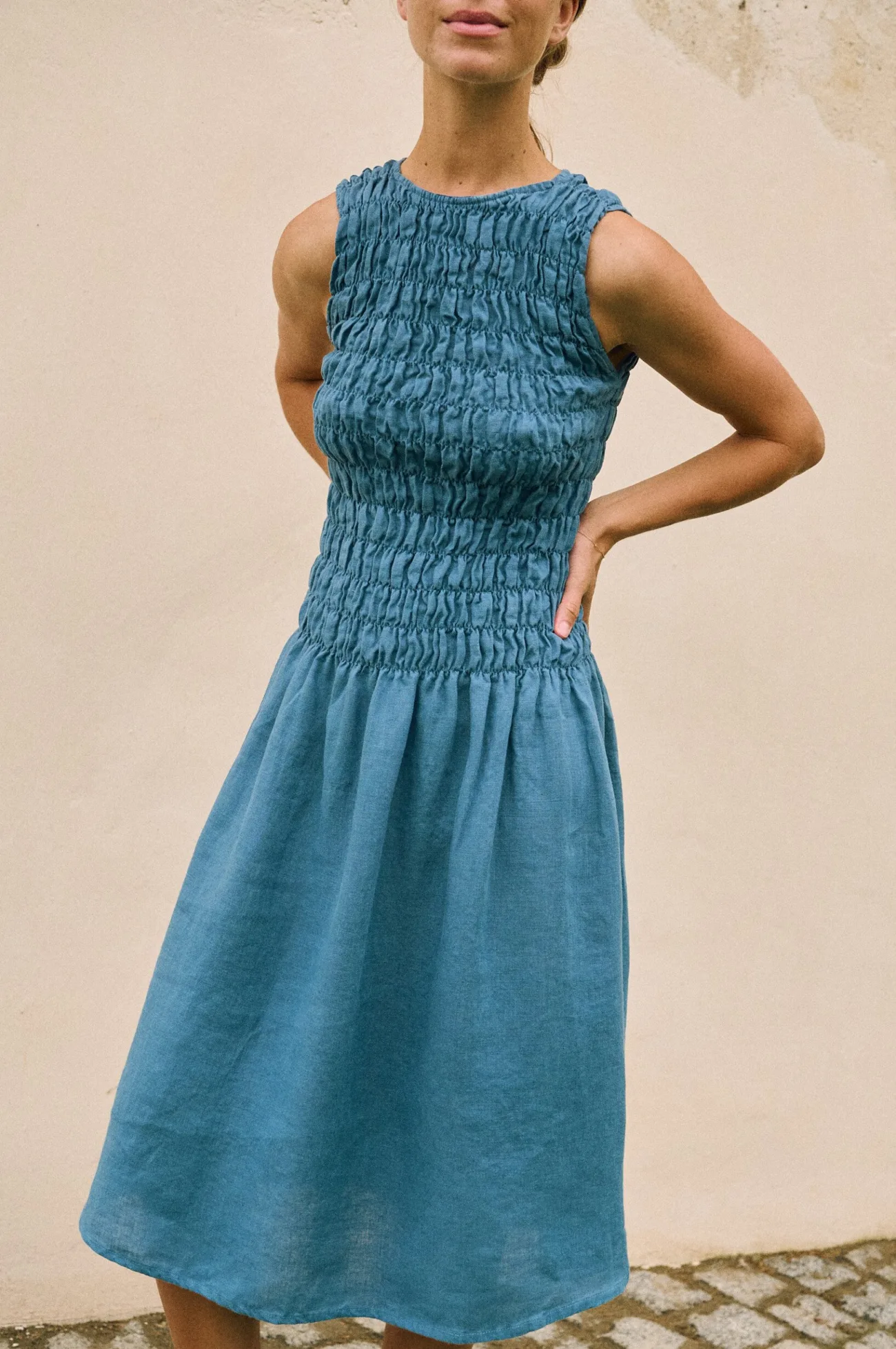 Model wearing a stellar blue linen dress featuring a smocked bodice, round neckline, and relaxed midi-length skirt