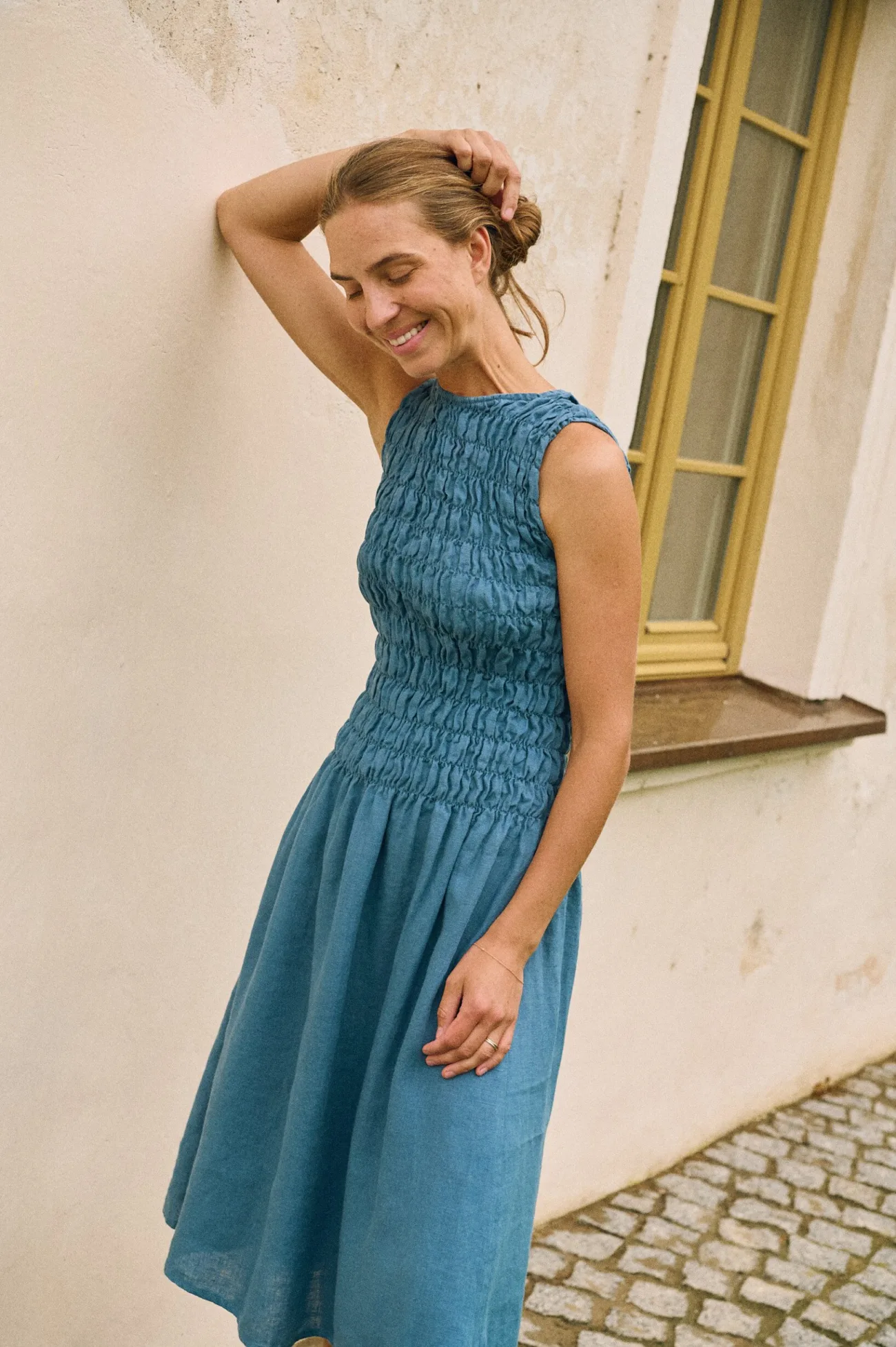 Model wearing a sleeveless stellar blue linen dress with smocked bodice, side view