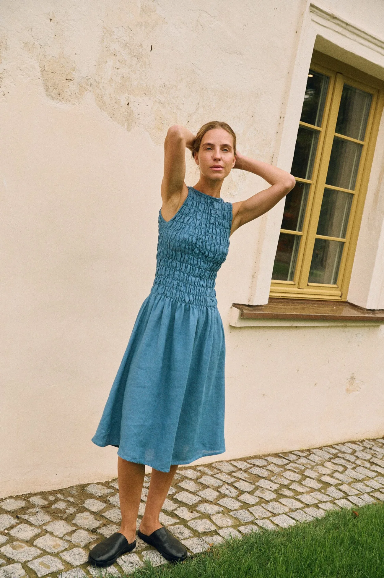 Model wearing a sleeveless stellar blue linen dress with a smocked bodice and midi-length skirt