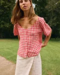 Woman wearing a red gingham linen button-front top with a curved neckline and short sleeves, paired with a natural linen cotton blend wrap skirt with adjustable tie waist