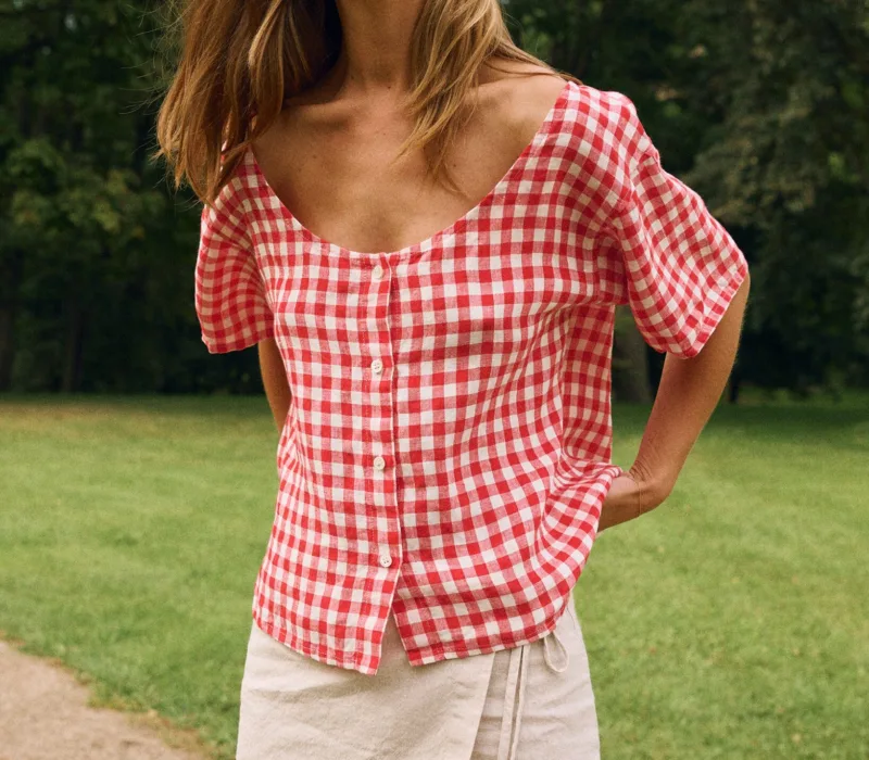 Woman wearing a red gingham linen button-front top with a curved neckline and short sleeves, paired with a natural linen cotton blend wrap skirt with adjustable tie waist