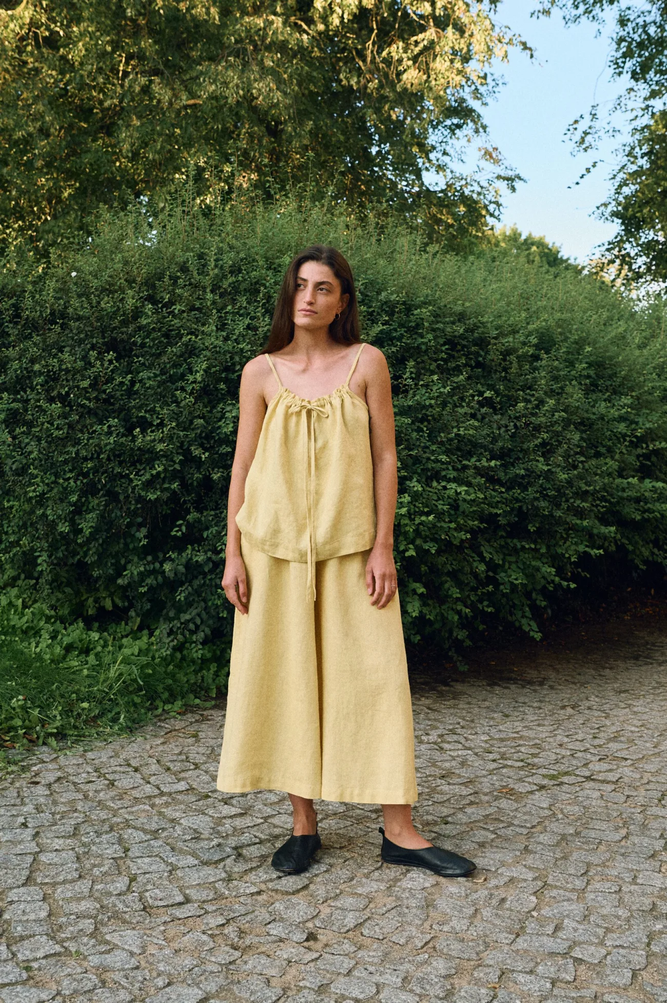 Butter yellow linen camisole top with adjustable drawstring neckline and thin straps, paired with wide-leg cropped linen trousers, made from breathable natural linen