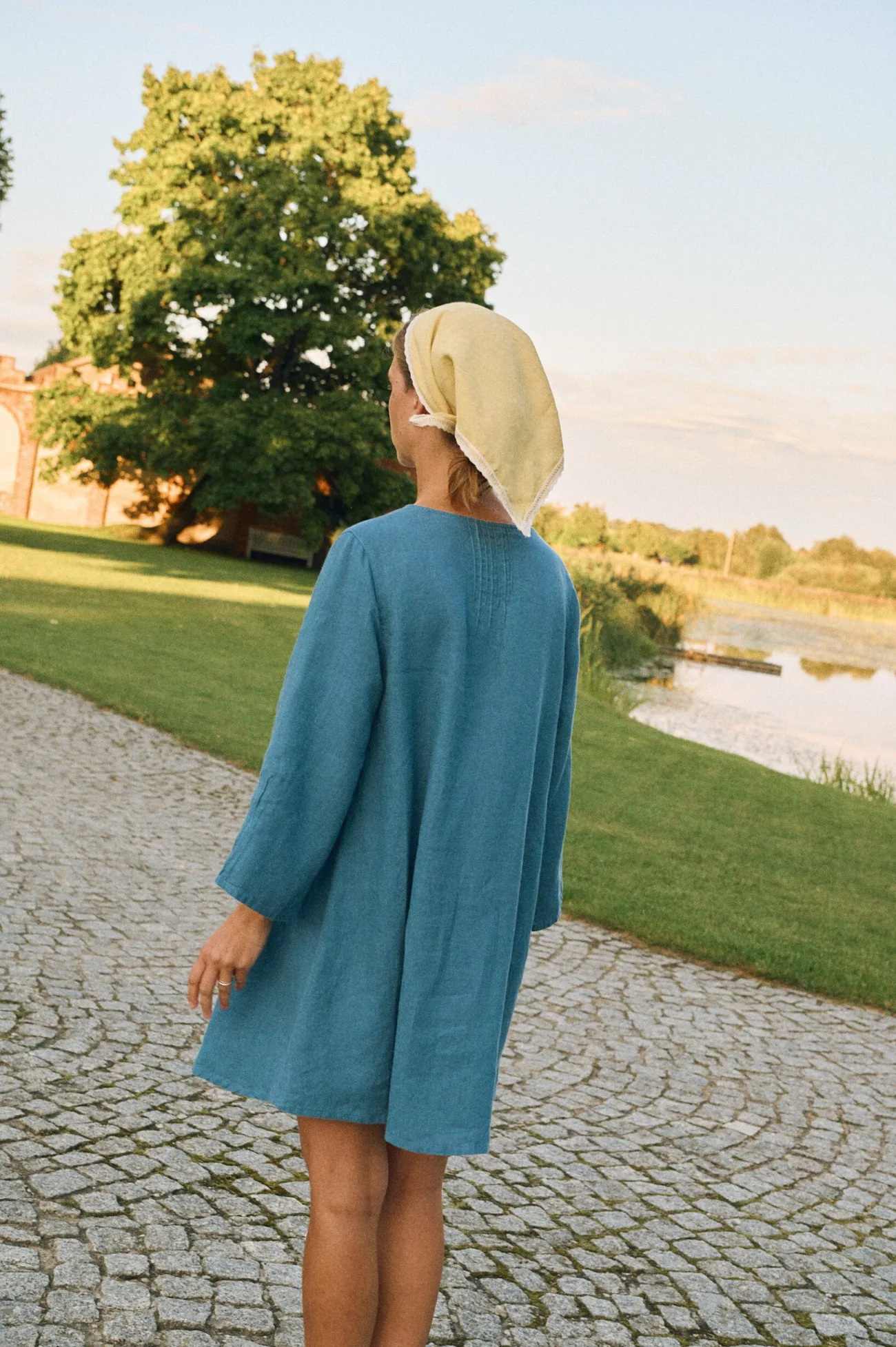 Back view of stellar blue linen mini dress with vertical stitching detail and relaxed fit, styled with butter headscarf