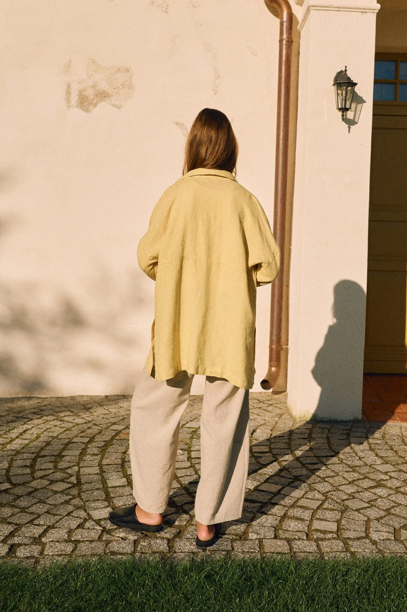 Back view of butter yellow linen shirt with relaxed drape styled with natural cotton-linen pants