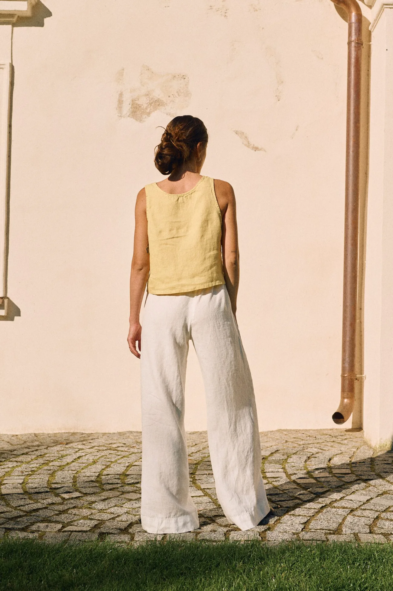 Back view of white linen wide-leg trousers with drawstring, paired with a butter yellow sleeveless linen top
