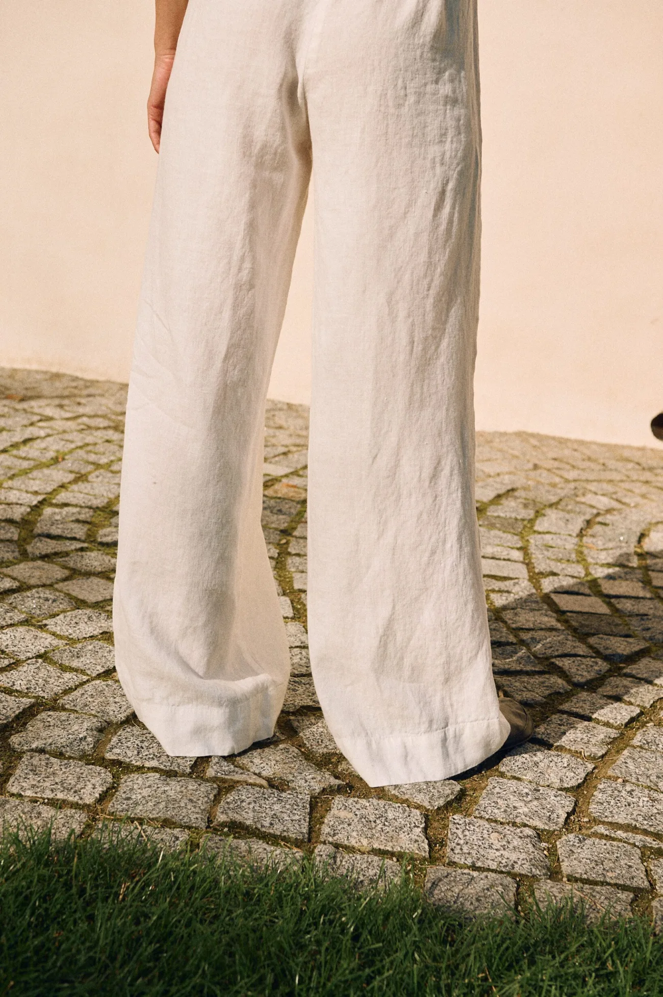 Back view of relaxed wide-leg linen trousers in milky white, featuring a soft drape and airy fabric