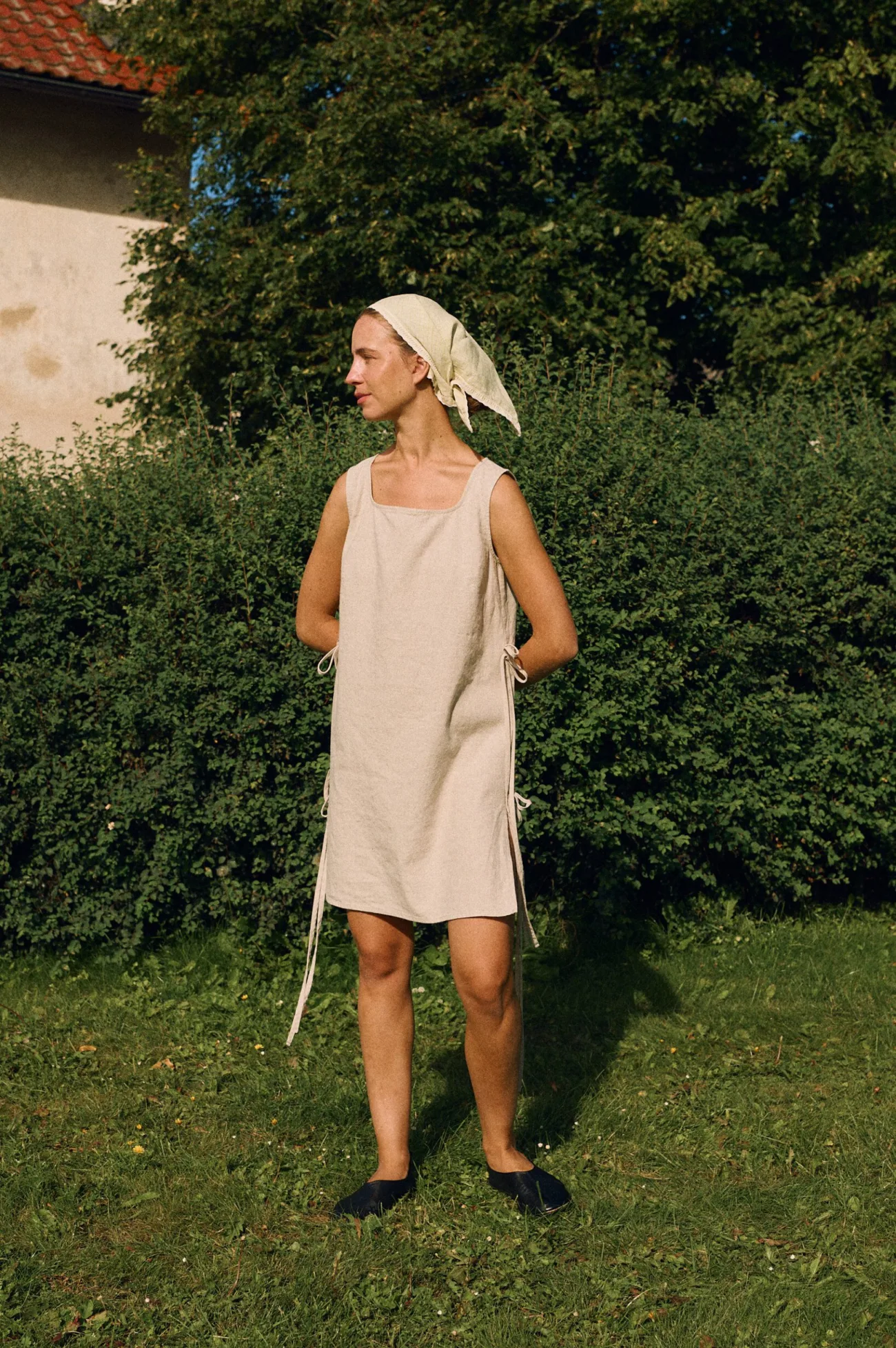 Sleeveless natural cotton blend dress with a relaxed fit, square neckline, and side ties, styled outdoors