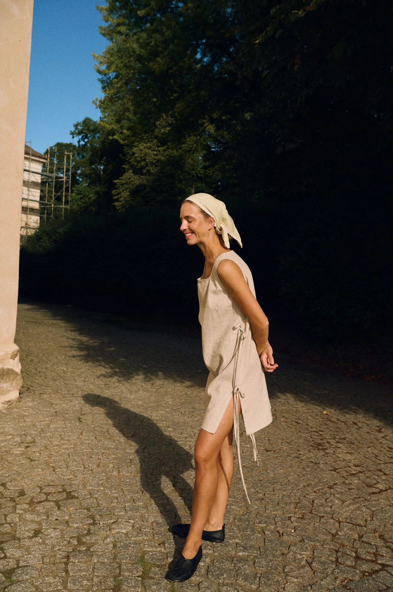 Model wearing a sleeveless natural cotton blend linen dress with side tie details, styled with a linen bandana in apple checks fabric with lace trim