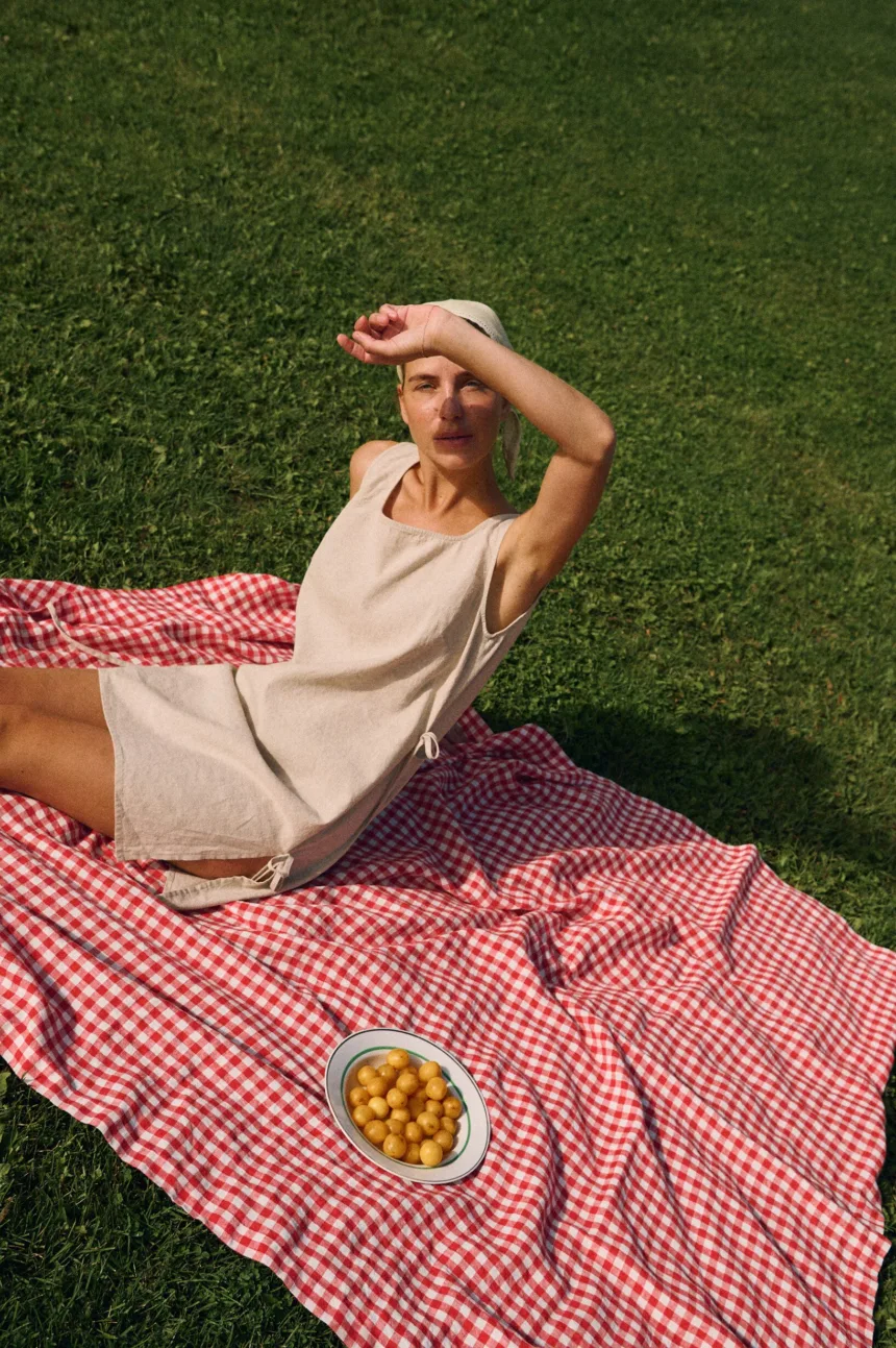 Model wearing a sleeveless natural cotton blend summer dress with side tie details, styled outdoors on a picnic blanket