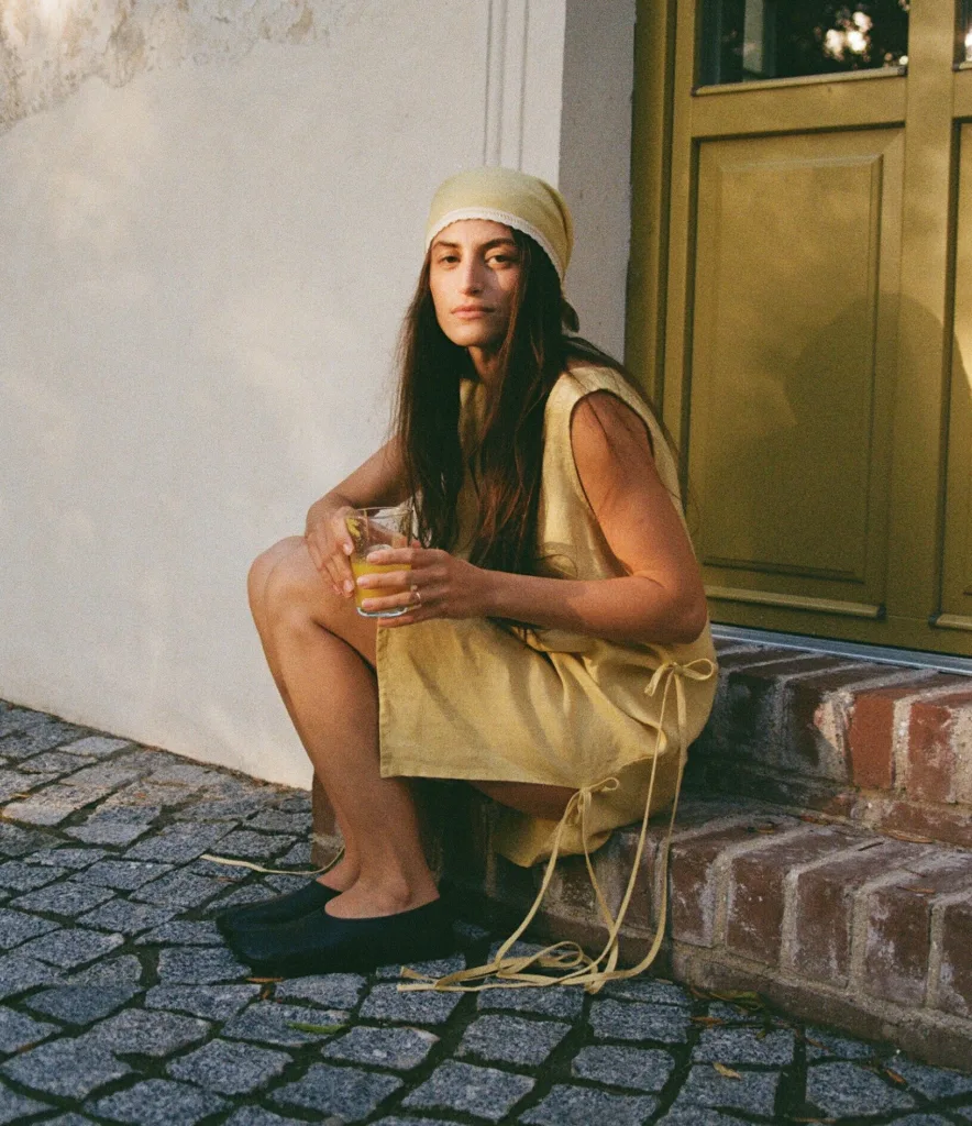 Woman seated outdoors in sleeveless butter yellow linen dress with side ties and matching headscarf