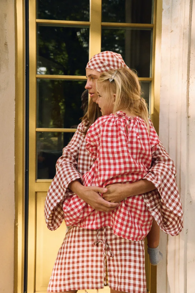 Woman wearing terracotta gingham linen dress holding child in red gingham linen dress