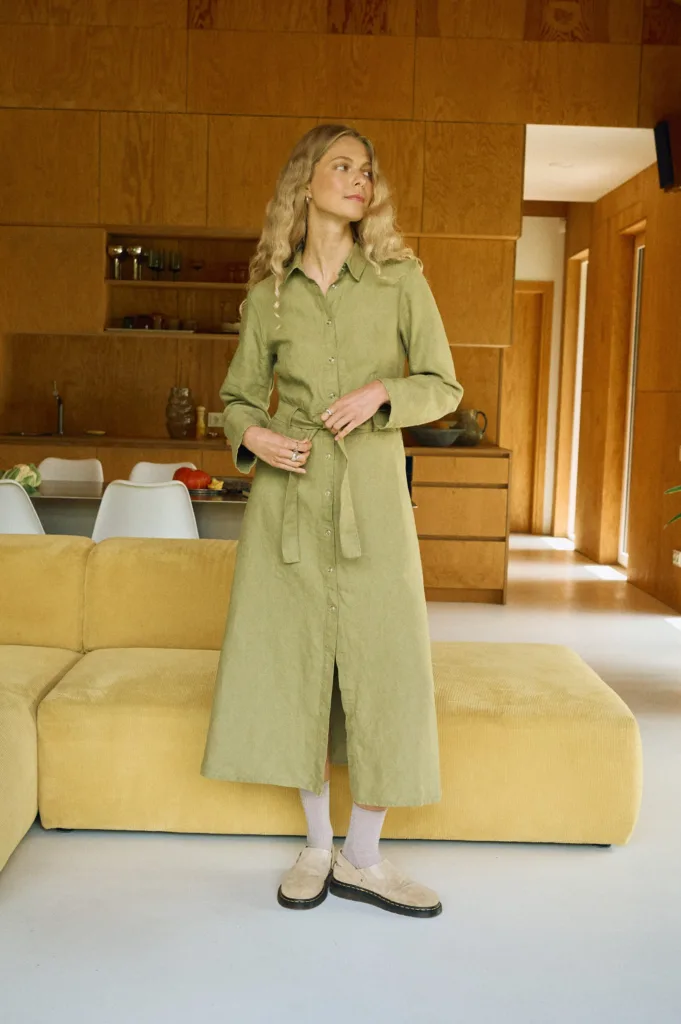 Front view of an olive heavy linen midi shirt dress with long sleeves, snap-front closure, and a self-tie belt that shapes the waist
