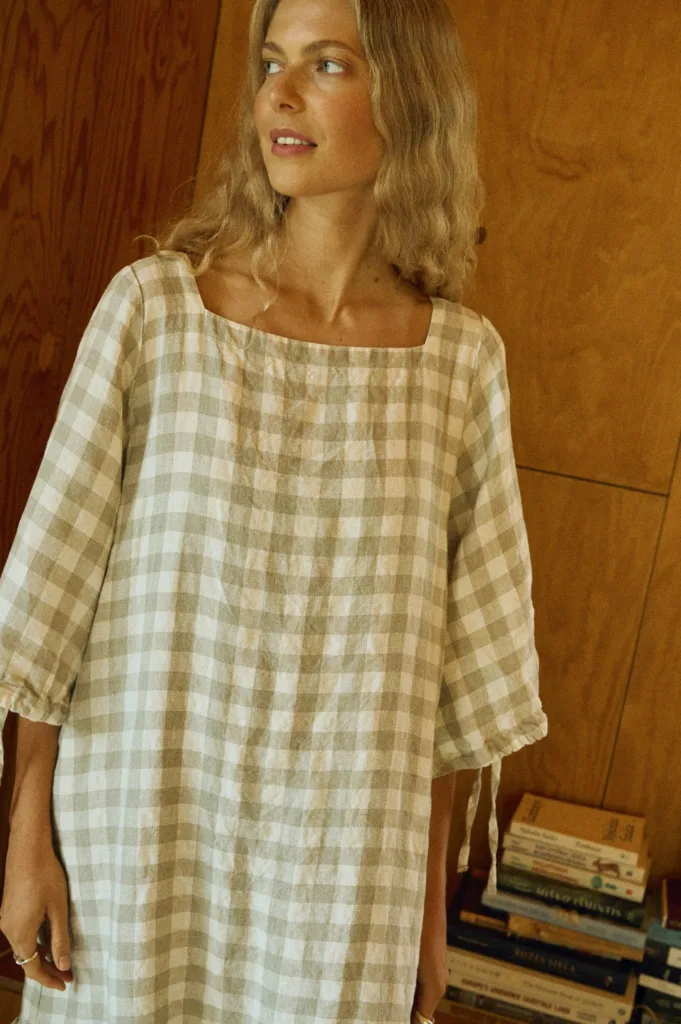 Close-up of a soft linen dress in large natural gingham, featuring a square neckline and gathered 3/4 sleeves with delicate ties