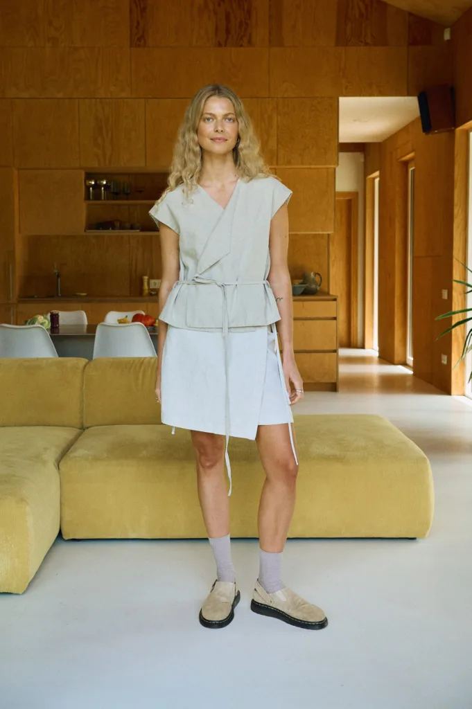 Woman wearing the natural linen cotton blend Tyra vest layered over the mini wrap skirt